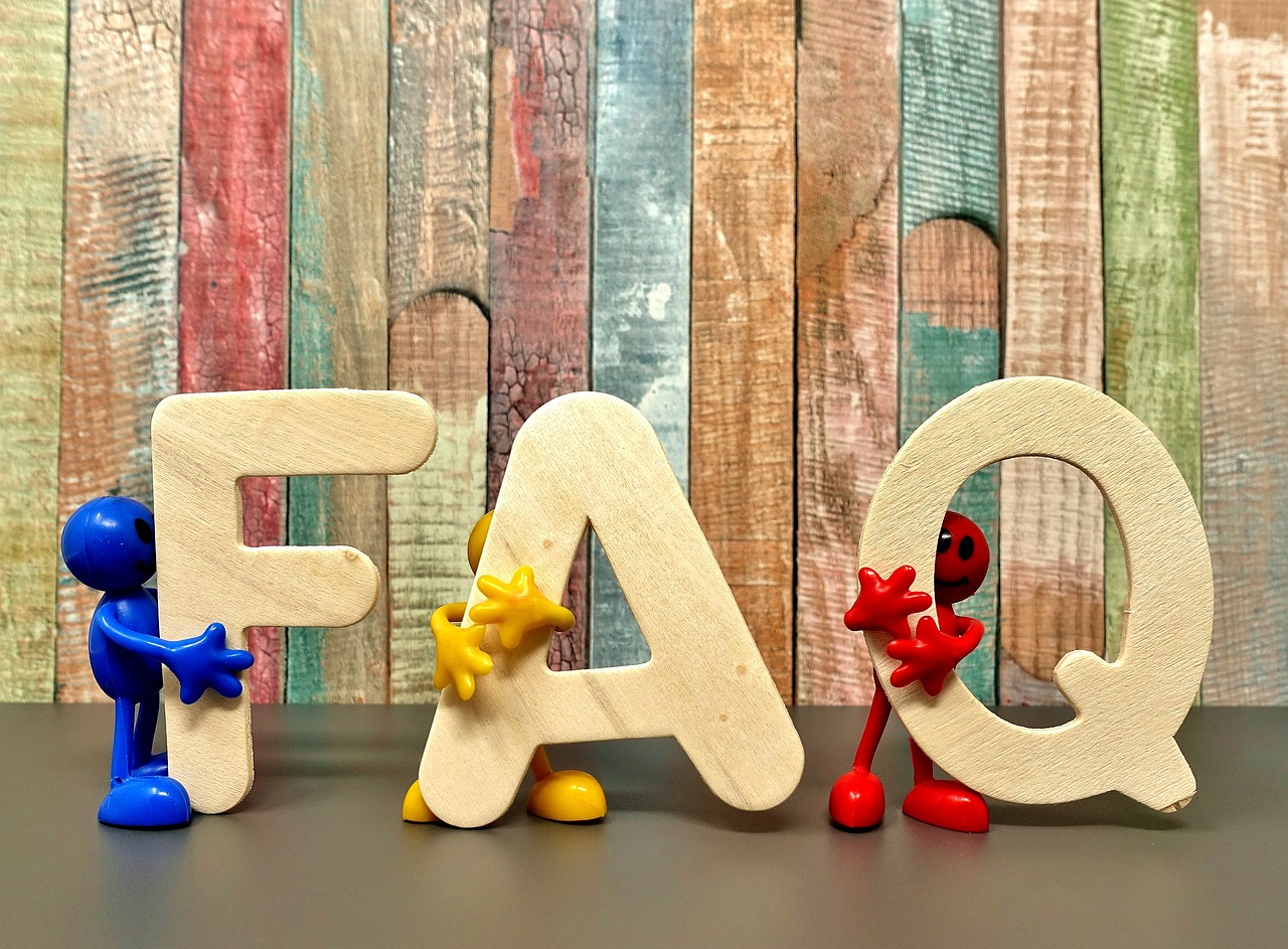 wooden letters F, A, Q being held up by small colorful plastic people with a reclaimed wood background